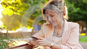 Attractive white woman blonde using a smartphone in park at sunny day