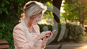 Attractive white woman blonde using a smartphone in park at sunny day