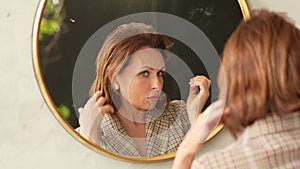 an attractive woman adjusts her hair at a round mirror.