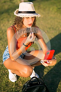 Attractive woman applying lip gloss looking at smart phone