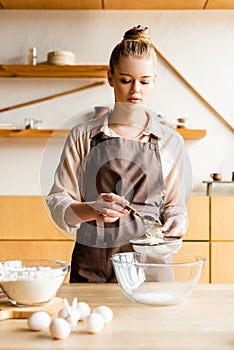 Attractive woman in apron sieving flour