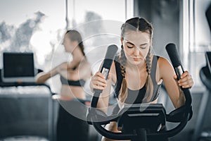 Attractive woman biking in the gym, exercising legs doing cardio workout cycling bikes. Fitness club with training exercise bikes