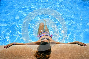 Attractive woman in bikini and sunglasses sunbathing leaning on edge of holidays resort swimming pool