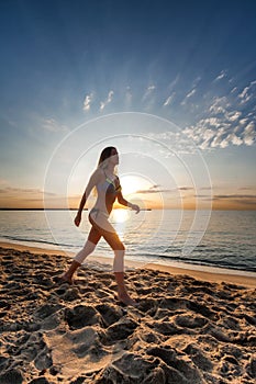 Attractive woman in bikini walking on sand on lonely beach