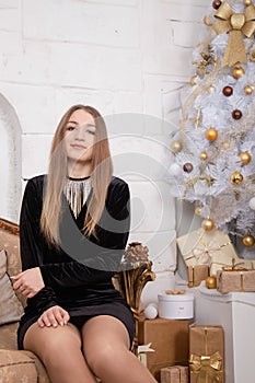 attractive woman in black dress sitting on a golden classic couch near white christmas tree. happy new year