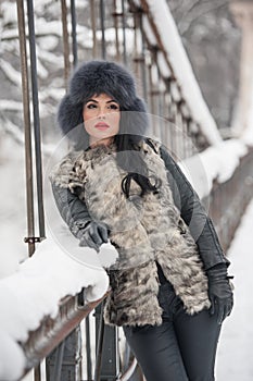 Attractive woman with black fur cap and gray waistcoat enjoying the winter. Side view of fashionable brunette girl posing