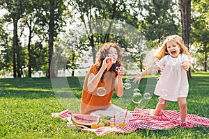 Attractive woman blowing sopa bubbles while girl playing with them in the park