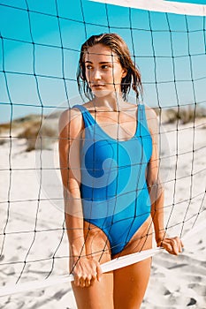 Attractive woman in blue bikini with tennis net on sandy beach.