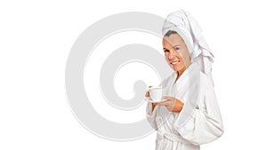 Attractive woman with brown eyes in a white towel on her head and a white robe, smiling, holding a cup of coffee in her hands