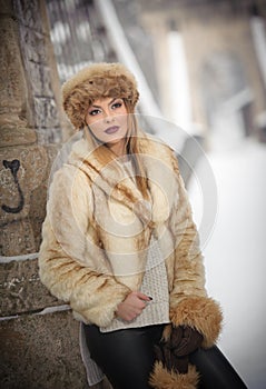 Attractive woman with brown fur cap and jacket enjoying the winter. Side view of fashionable blonde girl posing against bridge