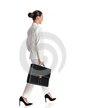 attractive woman with bun hair in suit holding bag and walking