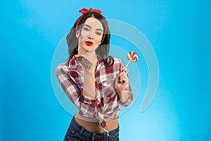 The attractive woman with a candy blowing an air kiss on the blue background.