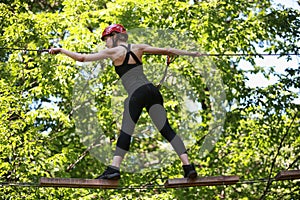 Attractive woman climbing in adventure rope park in safety equipment