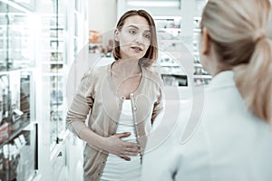 Attractive woman complaining to the druggist of her stomach ache.