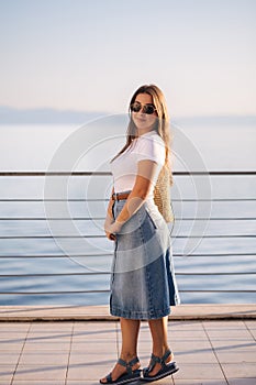 Attractive woman in denim style stand in front of sea landscape. Happy woman looking on sunset