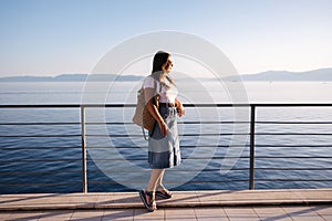 Attractive woman in denim style stand in front of sea landscape. Happy woman looking on sunset