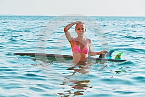 Attractive woman after dive in sea. Surfboard floating on water. Surfing sport, summer time and holiday trip concept