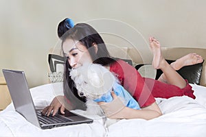 Attractive woman and dog use laptop on bed