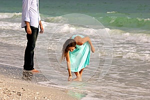 Attractive woman in dress stoops to pick up shell