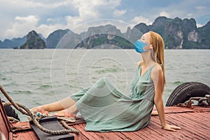 Attractive woman in a dress wearing a medical mask during COVID-19 coronavirus is traveling by boat in Halong Bay