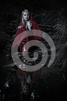 Attractive woman dressed a little red riding-hood cross stream in a dark forest with a lantern