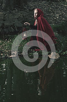 Attractive woman dressed a little red riding-hood cross stream in a dark forest with a lantern