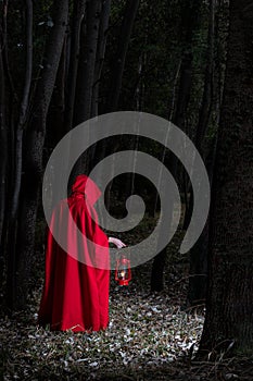 Attractive woman dressed a little red riding-hood walk in a dark forest with lantern