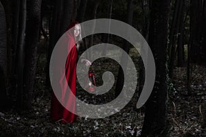 Attractive woman dressed a little red riding-hood walk in a dark forest with lantern