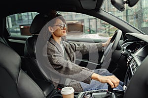 Attractive woman driving car in city with one hand on steering wheel and another on gear lever