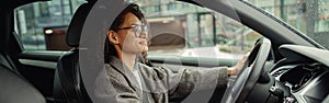 Attractive woman driving car in city with one hand on steering wheel and another on gear lever