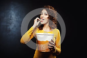 Attractive woman eating cheesy popcorn looking pleased and happy