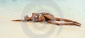 Attractive woman in fashionable brown bikini lying down on the sand, relaxing, sun tanning on caribbean beach. Travel destination