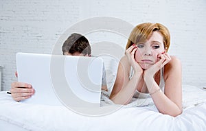Attractive woman feeling upset unsatisfied and frustrated in bed with his husband while the man work on computer laptop ignoring h
