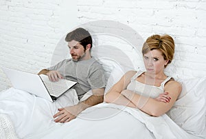 attractive woman feeling upset unsatisfied and frustrated in bed with his husband while the man work on computer laptop ignoring h