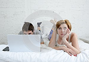 attractive woman feeling upset unsatisfied and frustrated in bed with his husband while the man work on computer laptop ignoring h