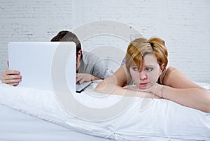 attractive woman feeling upset unsatisfied and frustrated in bed with his husband while the man work on computer laptop ignoring h