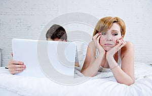 attractive woman feeling upset unsatisfied and frustrated in bed with his husband while the man work on computer laptop ignoring h