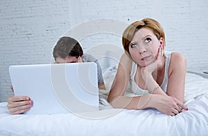 attractive woman feeling upset unsatisfied and frustrated in bed with his husband while the man work on computer laptop ignoring h