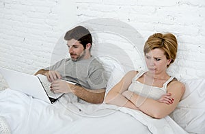 attractive woman feeling upset unsatisfied and frustrated in bed with his husband while the man work on computer laptop ignoring h