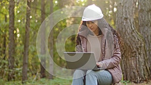 Attractive woman forestry engineer in protective helmet enters data into laptop takes reforestation action young