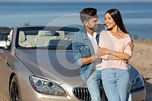 Attractive woman and handsome man leaning car and looking at each other