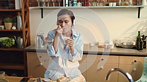 Woman eating yogurt in kitchen. Beautiful girl listening music in headphones.