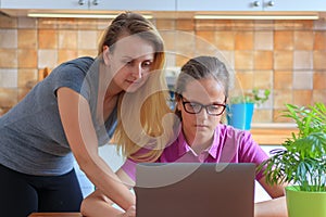 Attractive woman helping her teenage daughter to do her homework in kitchen