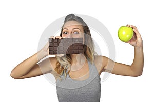 Attractive woman holding apple and chocolate bar in healthy fruit versus sweet junk food temptation