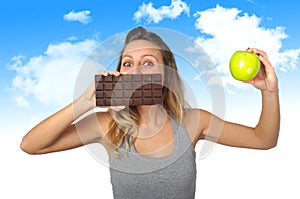 Attractive woman holding apple and chocolate bar in healthy fruit versus sweet junk food temptation