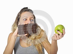 Attractive woman holding apple and chocolate bar in healthy fruit versus sweet junk food temptation