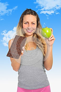 Attractive woman holding apple and chocolate bar in healthy fruit versus sweet junk food temptation