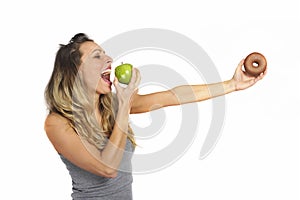 Attractive woman holding apple and chocolate donut in healthy fruit versus sweet junk food temptation