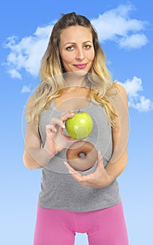 Attractive woman holding apple and chocolate donut in healthy fruit versus sweet junk food temptation