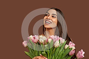 Attractive woman holding a bouquet of white and pink tulips on a brown background laughs and looks up. Copy space